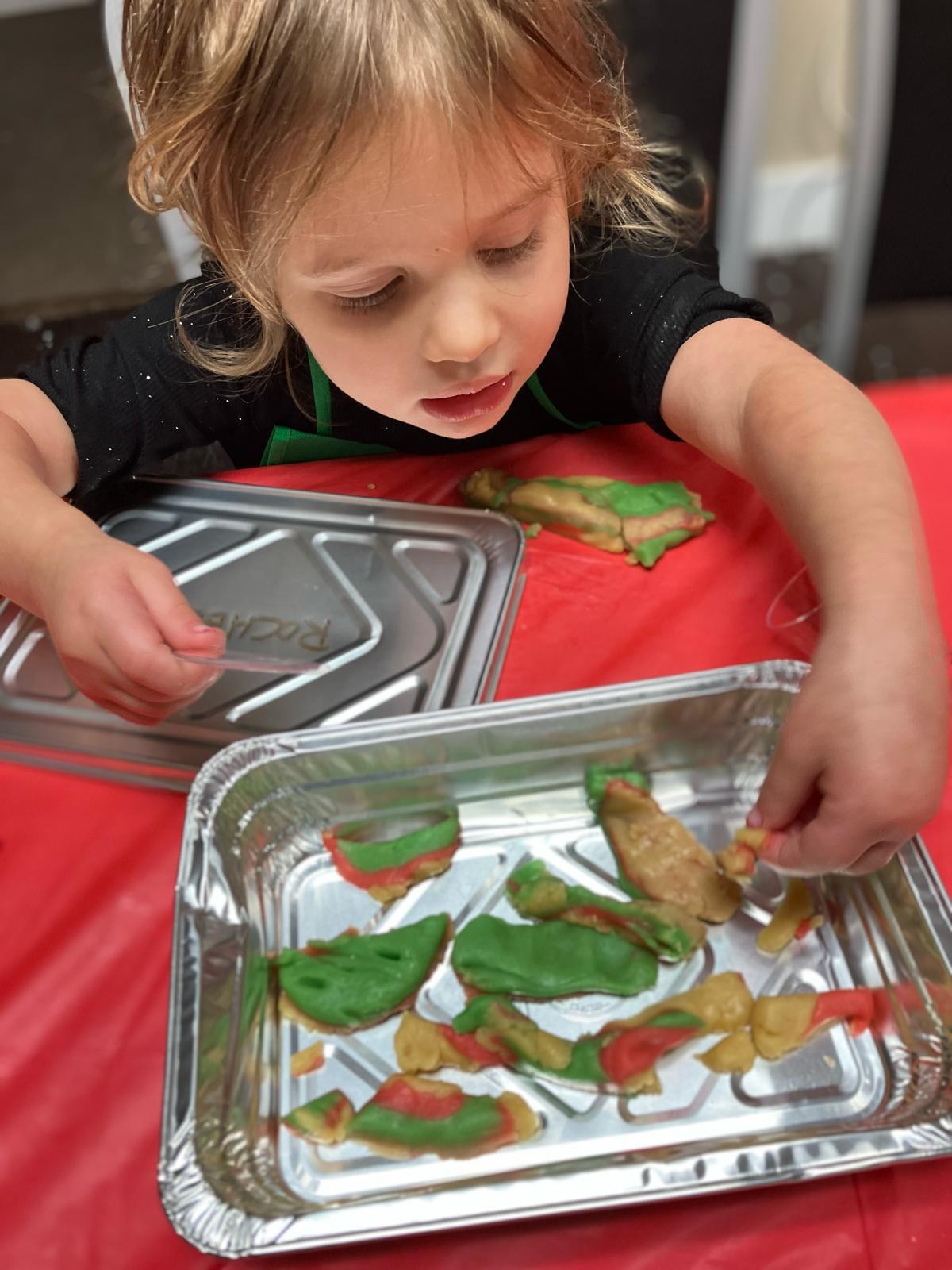 A child in an apron pressing coloured dough onto a foil tray.