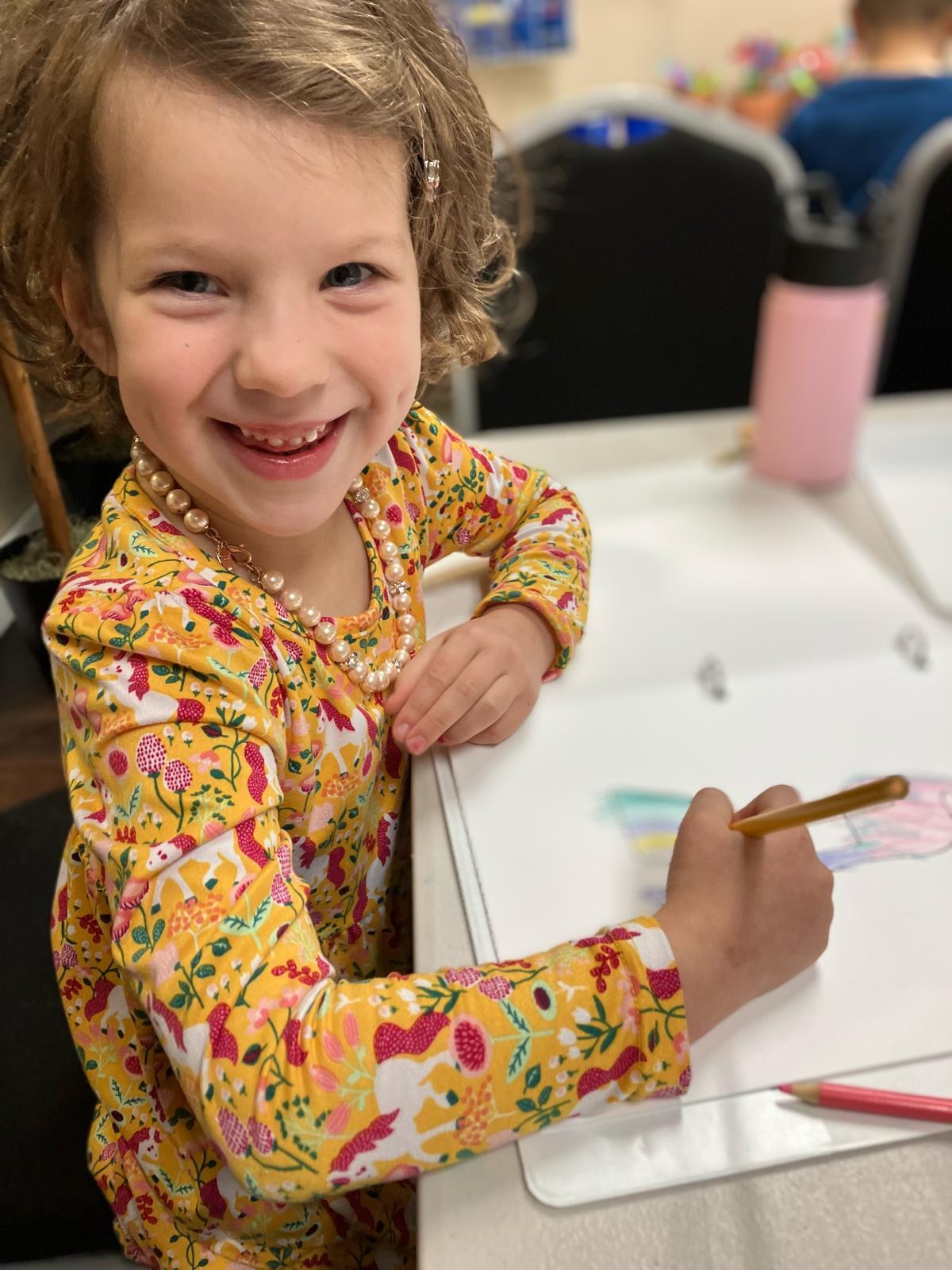 A child drawing at a table with coloured pencils.